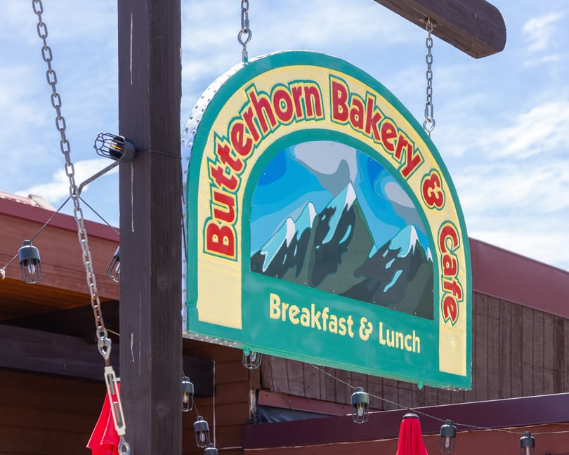 A colorful Butterhorn Bakery & Cafe sign with a mountain graphic hangs from a wooden post.