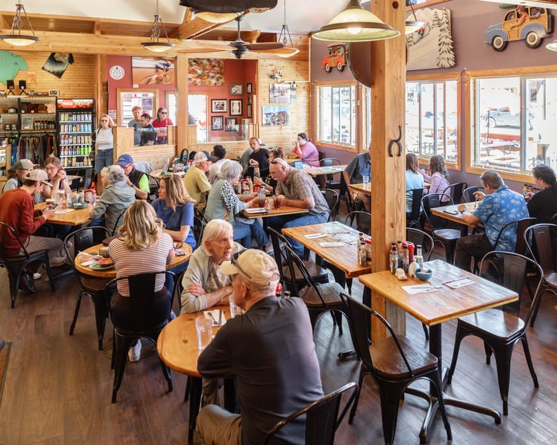 A bustling restaurant interior with many patrons seated at wooden tables, enjoying meals and conversation.