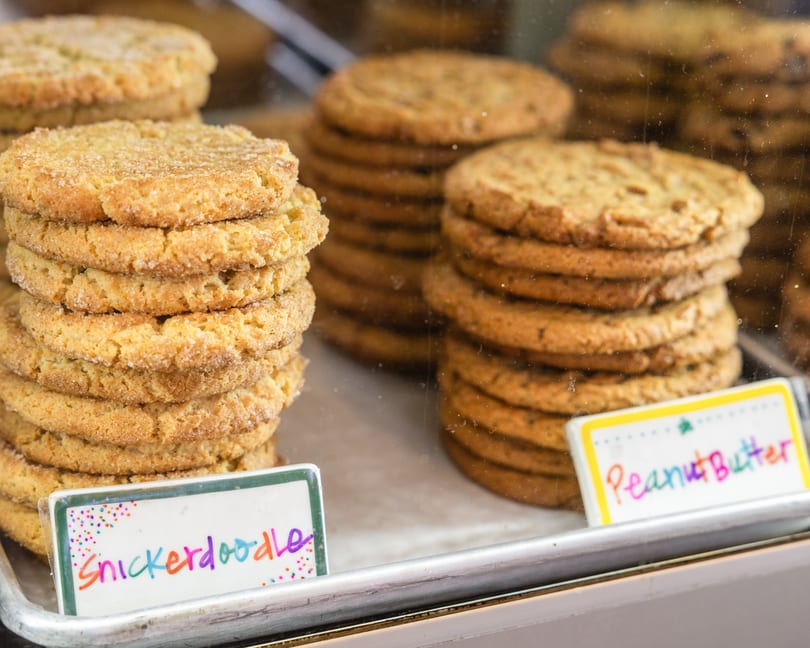 Stacks of Snickerdoodle and Peanut Butter cookies displayed in a bakery case.