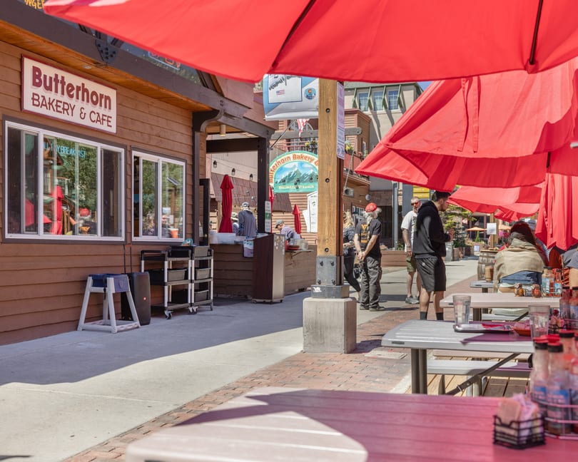 Outdoor dining area of Butterhorn Bakery & Cafe with red umbrellas, picnic tables, and people.