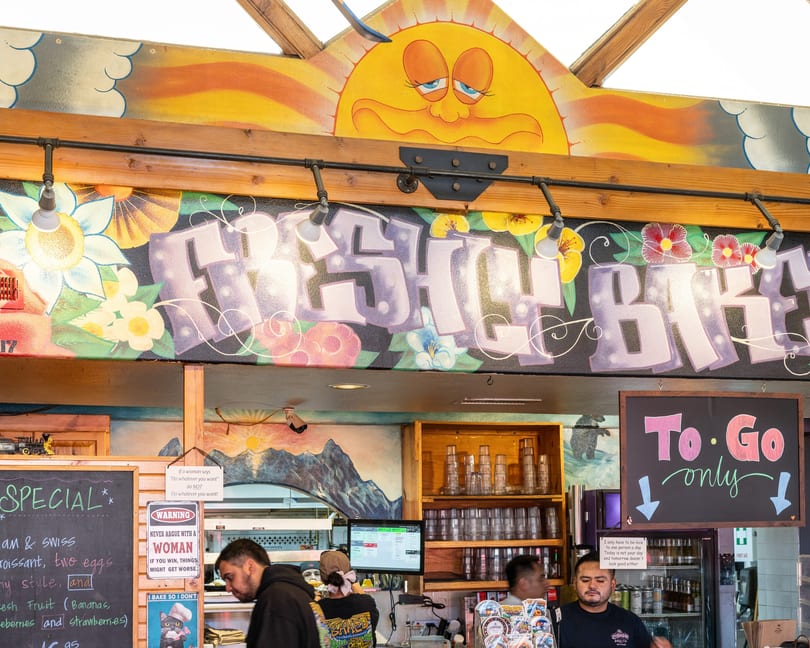 A vibrant, colorful mural with "FRESH BAKED" in graffiti-style letters above a bustling restaurant counter.