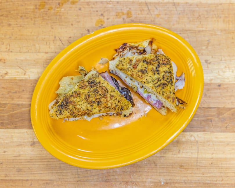 Two halves of a grilled sandwich with meat and cheese, served on a bright yellow plate.