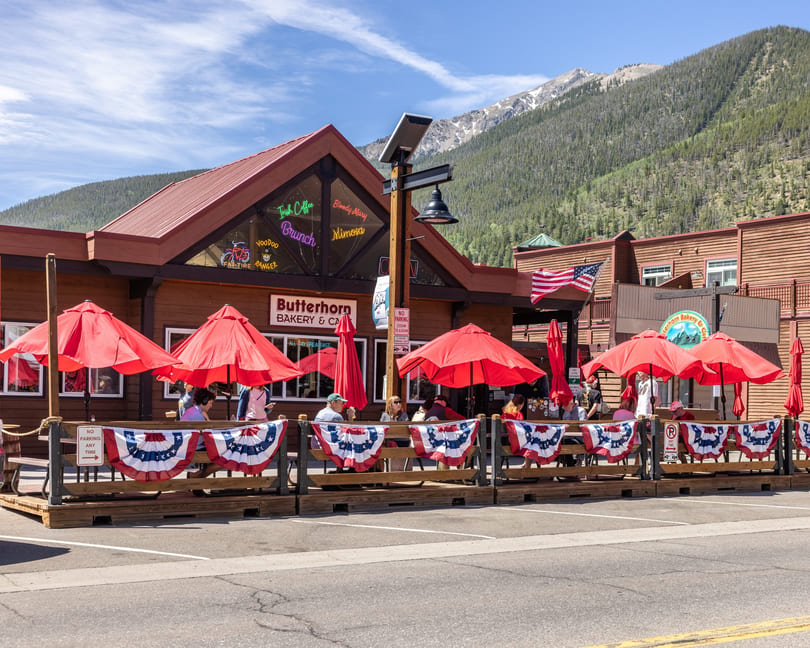 Butterhorn Bakery & Cafe with outdoor patio seating under red umbrellas, backed by mountains.