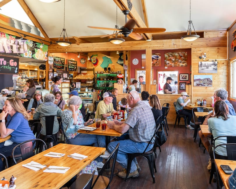 A busy, rustic restaurant interior with many patrons seated at wooden tables, enjoying meals and conversation.