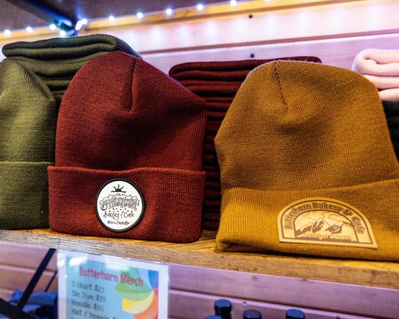 Butterhorn Bakery & Cafe branded beanies in red and mustard yellow on a wooden shelf.